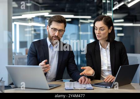Zwei Geschäftsleute diskutieren während eines Meetings mit Laptops und Dokumenten, die auf dem Tisch liegen. Eine helle, moderne Büroumgebung verbessert die Arbeitsatmosphäre. Stockfoto