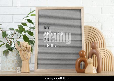 Brieftafel mit dem Satz My Dreams Come True, Pflanzen- und Dekorationselemente auf Holztisch in der Nähe der weißen Ziegelwand Stockfoto