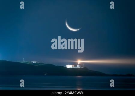 Ein Halbmond erleuchtet eine ruhige nächtliche Meereslandschaft und strahlt sein sanftes Leuchten über einen Leuchtturmstrahl. Die ruhige Szene ist perfekt zum Entspannen und Stockfoto