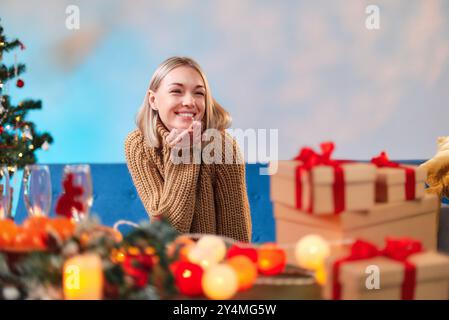 Frau schickt einen Luftkuss, während sie ihren Weihnachtstisch mit Geschenken und festlicher Dekoration vorbereitet. Stockfoto