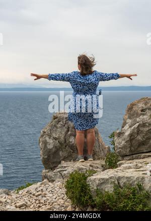 Freie Frau, die am Rande einer Klippe steht. Die Arme sind seitlich gegen Wind ausgespannt. Blick von hinten. Freiheit. Neu im Leben. Kopierbereich Stockfoto