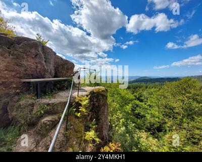 Felsiger Aussichtspunkt mit Bank mit Blick auf eine bewaldete Landschaft an einem klaren, sonnigen Tag in Thüringen. Stockfoto