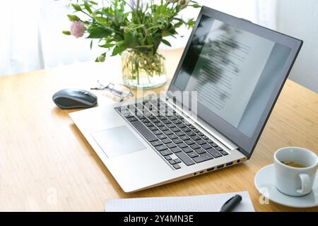 Laptop mit Text auf dem Bildschirm, Bürobedarf, Kaffee und Blumen auf einem Holzschreibtisch, Arbeitsplatz eines Autors, Studenten oder Erstellers von Inhalten, Kopierraum, Stockfoto