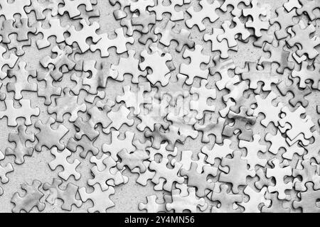Eine Nahaufnahme verstreuter Puzzleteile in Schwarz-weiß. Die Stücke sind nach dem Zufallsprinzip angeordnet, was ein Gefühl von Chaos und Unvollständigkeit schafft Stockfoto