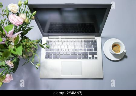 Silberfarbener Laptop auf einem grauen Schreibtisch mit Blumenstrauß und Kaffeetasse, Arbeitsplatz oder Home Office, Draufsicht von oben, Kopierraum, s Stockfoto