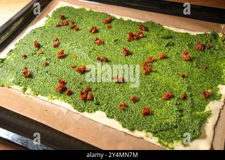 Blätterteig mit selbstgemachtem grünem Pesto und getrockneten Tomaten auf Backpapier und einem Blech, um Finger Food Party Snacks in Mediterra zu machen Stockfoto