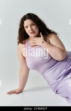 Eine atemberaubende Frau in Übergröße zeigt ihre Schönheit, während sie sich lässig in weichem Lavendel entspannt. Stockfoto