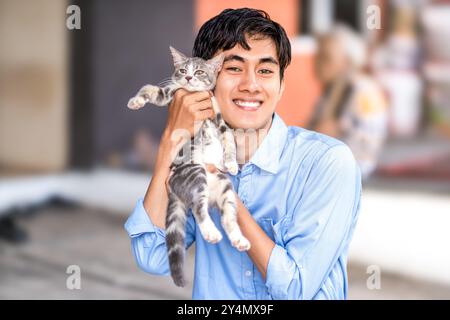 Ein Kerl lächelt, während er seine Katze umarmt. Schöne Männer und ein süßes Kätzchen. Stockfoto