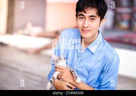 Ein Kerl lächelt, während er seine Katze umarmt. Schöne Männer und ein süßes Kätzchen. Stockfoto