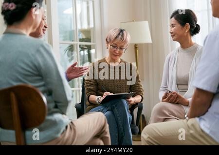 asiatische Beraterin, die eine Diskussionsrunde für eine Gruppe von Senioren leitet Stockfoto