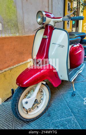 Ein wunderschön restaurierter Lambretta 150 LI Roller mit einem rot-weißen Farbschema, parkt an einer bunten Wand. Stockfoto