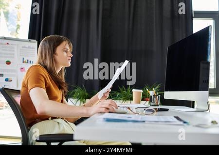 Der junge, nicht binäre Mensch analysiert Dokumente, während er an einem Schreibtisch im Büro sitzt. Stockfoto