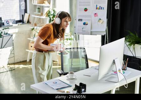 Diese junge, nicht binäre Person konzentriert sich intensiv, während sie in ihrer lebhaften Büroumgebung arbeitet. Stockfoto