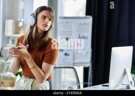 Eine junge, nicht binäre Person hört aufmerksam zu, während sie an ihrem Schreibtisch in einem Büro arbeitet. Stockfoto