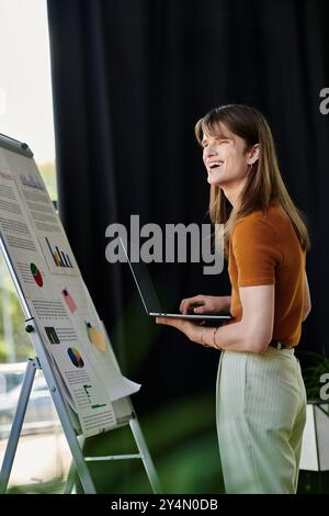 Eine junge, nicht binäre Person greift mit einem Laptop in Berührung, während sie farbenfrohe Diagramme und Daten präsentiert. Stockfoto