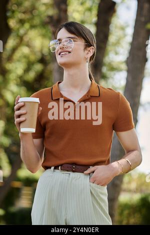 In einem Bürogarten lächelt eine junge, nicht binäre Person, schlürft Kaffee und nimmt Kreativität wahr. Stockfoto