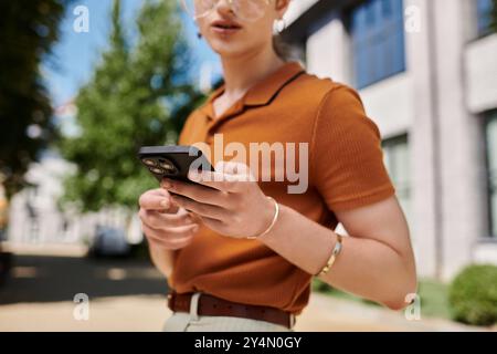 Eine Person greift mit ihrem Smartphone in Verbindung, während sie von Grün und moderner Architektur umgeben ist. Stockfoto