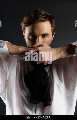 Ein eleganter Gentleman zeigt eine kühne Pose, verdeckt sein Gesicht mit Händen und strahlt Charme aus. Stockfoto