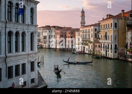 Blick von der Rialto-Brücke auf Gondoliere, die bei Sonnenuntergang auf Booten im Canale Grande von Venedig in Italien rudern Stockfoto