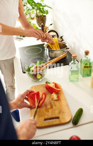 In einer hellen Küche hackt ein glückliches Paar buntes Gemüse und lacht und liebt bei einem Salat. Stockfoto