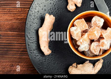 Schüssel mit kandierten Ingwerstücken und Ingwerwurzeln, Ingwerdessert auf alten rustikalen Holztisch. Stockfoto