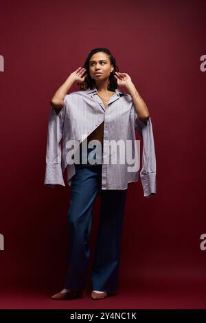 Eine junge afroamerikanische Frau mit Zöpfen posiert stilvoll in einem Studio und zeigt ihr trendiges Outfit und Selbstvertrauen. Stockfoto