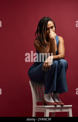 Eine junge afroamerikanische Frau mit geflochtenen Haaren posiert auf einem Stuhl und zeigt eine stilvolle und besinnliche Stimmung. Stockfoto