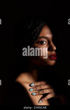 Eine stilvolle junge Frau präsentiert ihre Zöpfe und ihre auffälligen roten Lippen in einem dramatischen Studio-Setting. Stockfoto