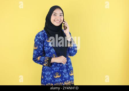 Fröhliche indonesische Regierungsangestellte, die Baju Korpri trägt, telefoniert oder telefoniert, mit Blick auf die Kamera. Stockfoto