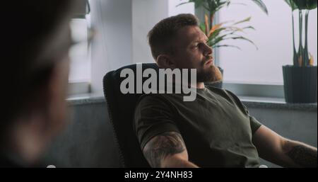 Depressiver Militärmann in Tarnung mit PTBS sitzt im Stuhl, teilt Gefühle mit Psychotherapeuten oder Psychologen auf Rehabilitationstherapie-Sitzung. Posttraumatische Belastungsstörung. Über die Schulter. Stockfoto