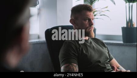 Depressiver Militärmann in Tarnung mit PTBS sitzt im Stuhl, teilt Gefühle mit Psychotherapeuten oder Psychologen auf Rehabilitationstherapie-Sitzung. Posttraumatische Belastungsstörung. Über die Schulter. Stockfoto