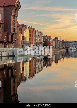 Historischer Gdańsk Crane ikonischer mittelalterlicher Hafenkran bei Sonnenaufgang, in goldenes Licht getaucht neben lebendiger traditioneller Architektur, polnisches Symbol Stockfoto