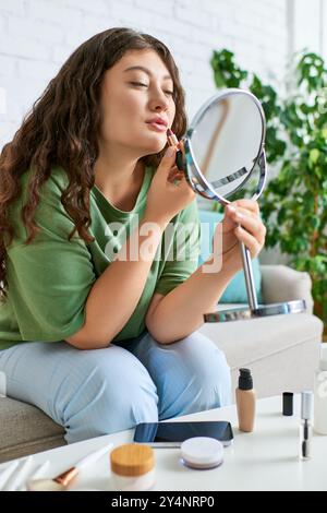 Eine junge Frau trägt Lippenstift, während sie in ihrem Wohnzimmer sitzt und von Kosmetikprodukten umgeben ist. Stockfoto