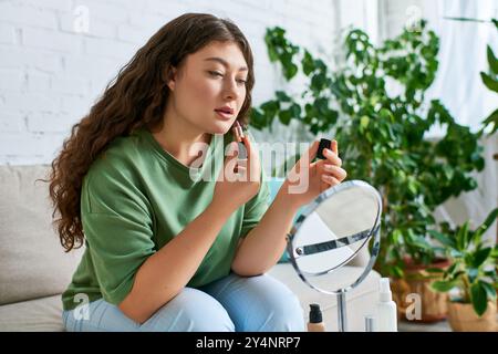 Eine Frau mit lockigen Haaren in lässigem Outfit trägt Lippenstift auf, während sie von Kosmetikprodukten umgeben ist. Stockfoto