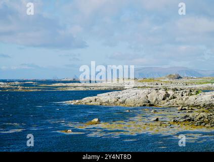 Eine zerklüftete felsige Küste auf Andøya, Nordnorwegen, mit fernen Bergen unter einem bewölkten Himmel und Wellen, die entlang der Küste krachen Stockfoto