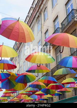 Farbenfrohe Regenschirme hängen über einer Straße vor einem historischen Gebäude und schaffen eine lebendige und künstlerische Installation. Stockfoto