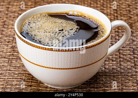 Eine Tasse schwarzen Kaffee. Hoher Winkel von heißem schwarzem Kaffee mit Luftblasen in schöner brauner Keramikschale auf dunkler Tischmatte. Stockfoto