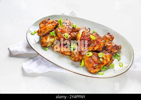 Hausgemachte Hähnchenflügel nach asiatischer Art mit grünen Zwiebeln auf Servierteller Stockfoto