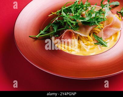 Spaghetti mit Schinken und Rucola auf rotem Teller Stockfoto