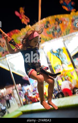 Ein kleines Kind springt fröhlich auf einem Bungy-Trampolin in Sanlucar de Barrameda während eines unterhaltsamen Abends. Stockfoto