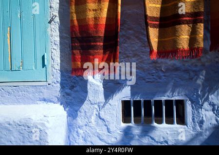 Farbenfrohe Teppiche hängen vor den Geschäften in der lebhaften Stadt Chefchaouen, die lokale Handwerkskunst und Kultur zeigen. Stockfoto