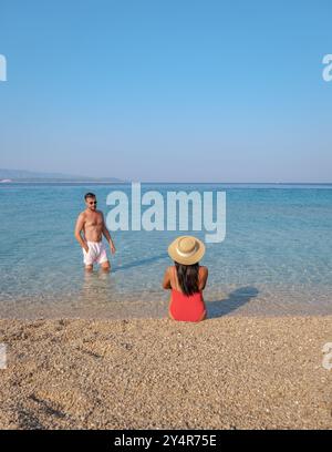 Auf der Insel Brac, Kroatien, entfaltet sich ein sonniger Nachmittag, während ein Mann durch kristallklares Wasser waten, während sich eine Frau in rotem Badeanzug am Ufer entspannt und die Ruhe des Augenblicks genießt. Stockfoto