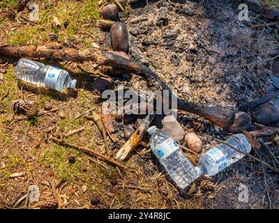 Entsorgte Plastikwasserflaschen und die Überreste eines offenen Feuers in trockener Landschaft. Stockfoto