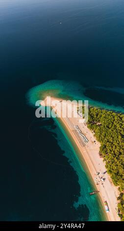 Goldener Sand erstreckt sich entlang der Küste von Brac Island, wo azurblaues Wasser auf üppiges grünes Laub trifft. Besucher sonnen sich in der Sonne und genießen die Ruhe dieses Paradieses am Meer. Zlatni Rat Beach Kroatien Stockfoto