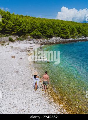 Ein paar gemütliche Spaziergänge Hand in Hand entlang des Kieselstrandes von Brac Island, umgeben von üppigem Grün und der glitzernden Adria unter einem hellblauen Himmel, genießen Sie einen friedlichen Sommermoment. Stockfoto