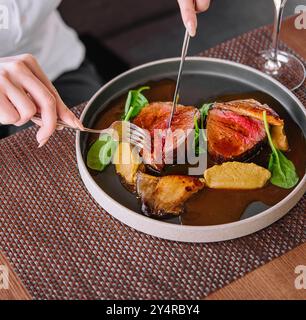 Weibliche Hände halten Gabel und Messer und schneiden Ente mit Wein Stockfoto