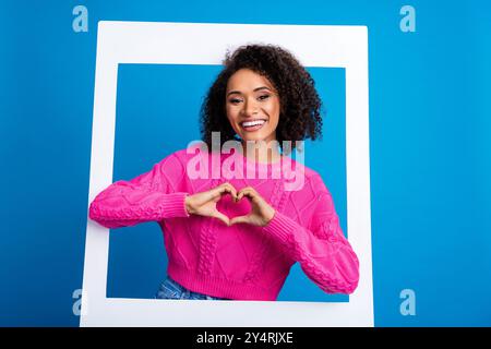 Foto-Porträt der schönen jungen Dame Instant Fotorahmen Herz Geste gekleidet stilvolles rosa Kleid isoliert auf blauem Farbhintergrund Stockfoto