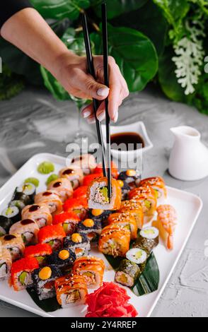 Nahaufnahme einer Person, die Essstäbchen verwendet, um eine Sushi-Rolle von einer verschiedenen Platte zu holen Stockfoto