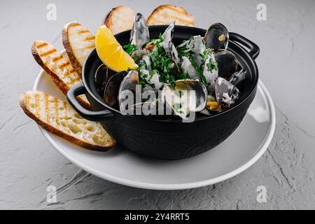 Schüssel mit gedämpften Muscheln garniert mit Kräutern, serviert mit gegrilltem Brot und Zitronenscheiben Stockfoto