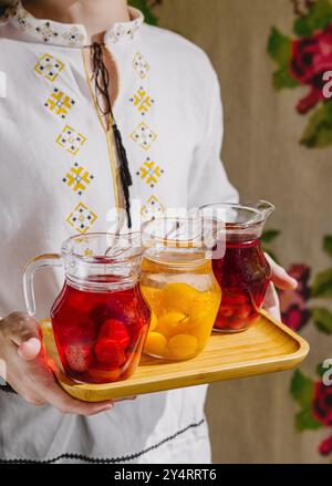 Die Person stellt drei Krüge mit erfrischendem, mit Früchten angereichertem Wasser auf einem Holztablett vor Stockfoto